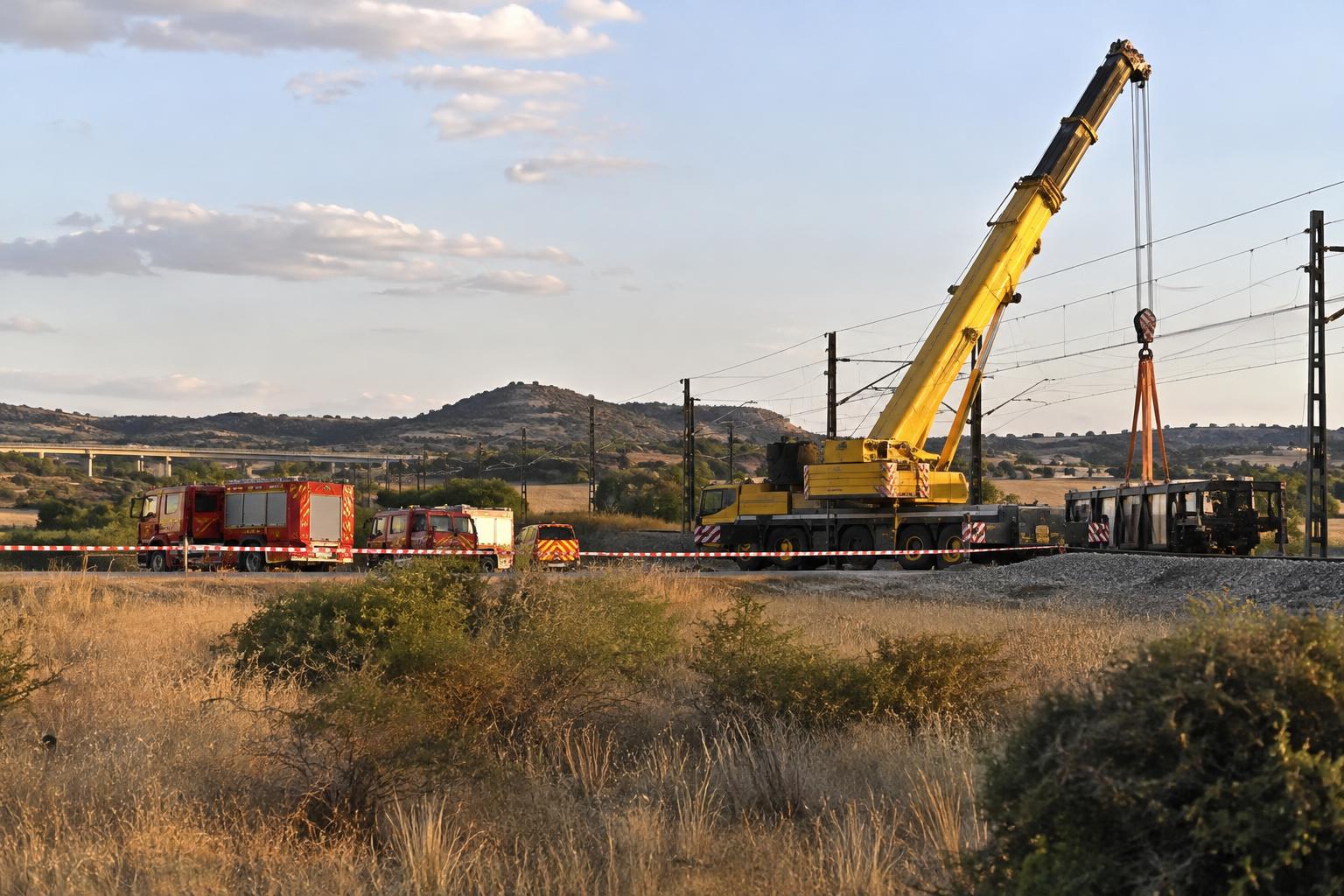 Exterior de un operativo de emergencia ferroviaria en un entorno rural español, con una grúa pesada junto a las vías, vehículos de bomberos y un perímetro de seguridad, sin víctimas visibles ni personas reconocibles.