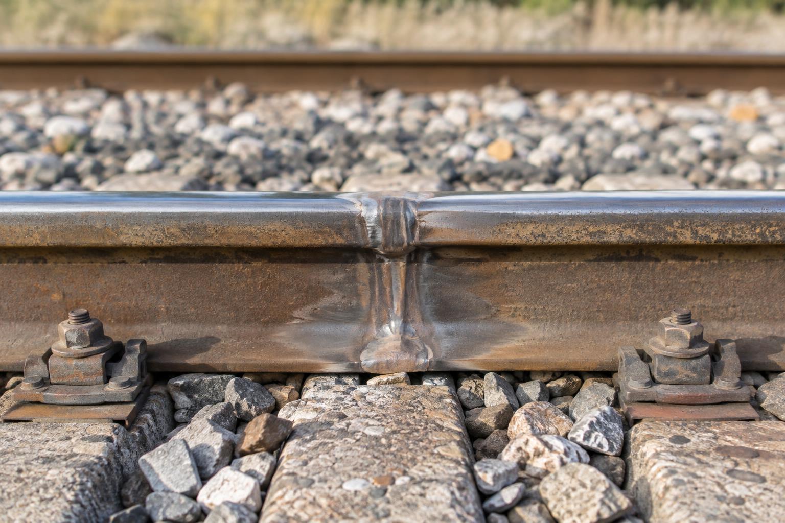 Detalle realista de un tramo de raíl ferroviario y su soldadura sobre balasto, en una vía sin circulación, con luz natural y sin personas ni trenes visibles.