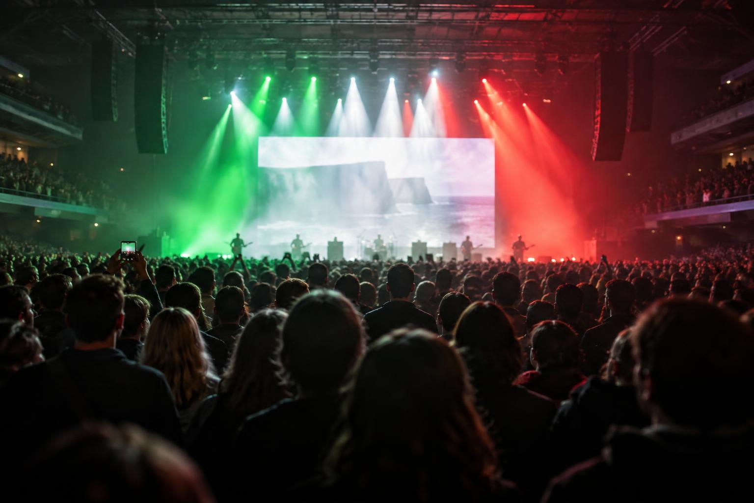 Interior de un gran recinto de conciertos en Dublín, con público visto de espaldas, escenario iluminado en rojo, verde y blanco y una gran pantalla al fondo sin rostros reconocibles.