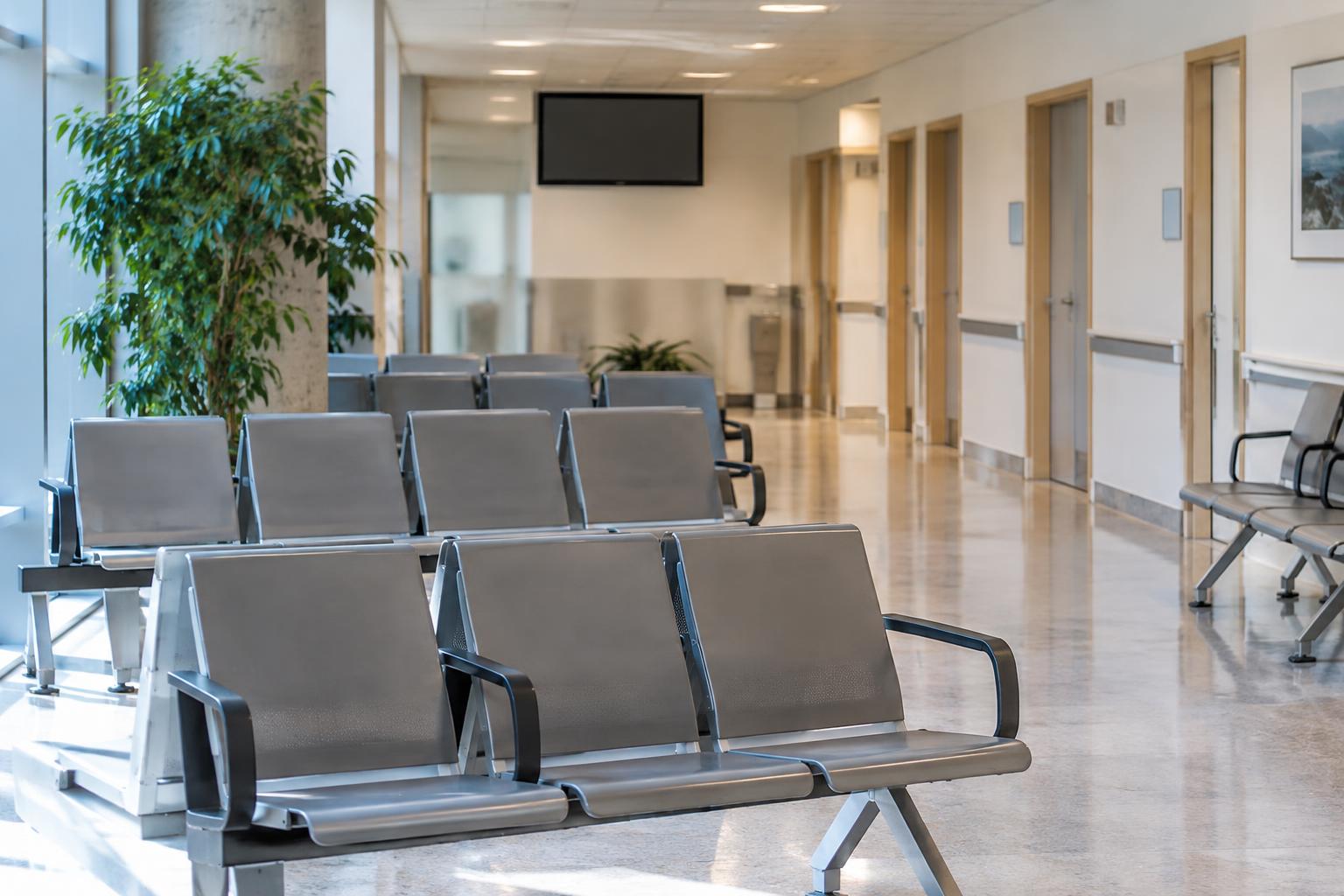 Sala de espera de un hospital público español, con filas de sillas, puertas de consultas y un panel de turnos al fondo, sin personas reconocibles ni datos personales visibles.