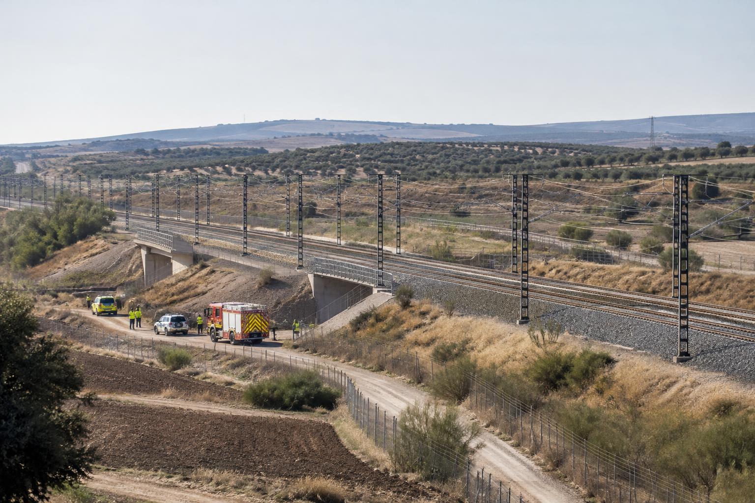 Vista general ilustrativa de una vía de alta velocidad en un paisaje rural de Toledo, con vehículos de emergencia junto a un acceso ferroviario y personal a distancia, sin personas reconocibles ni víctimas visibles.